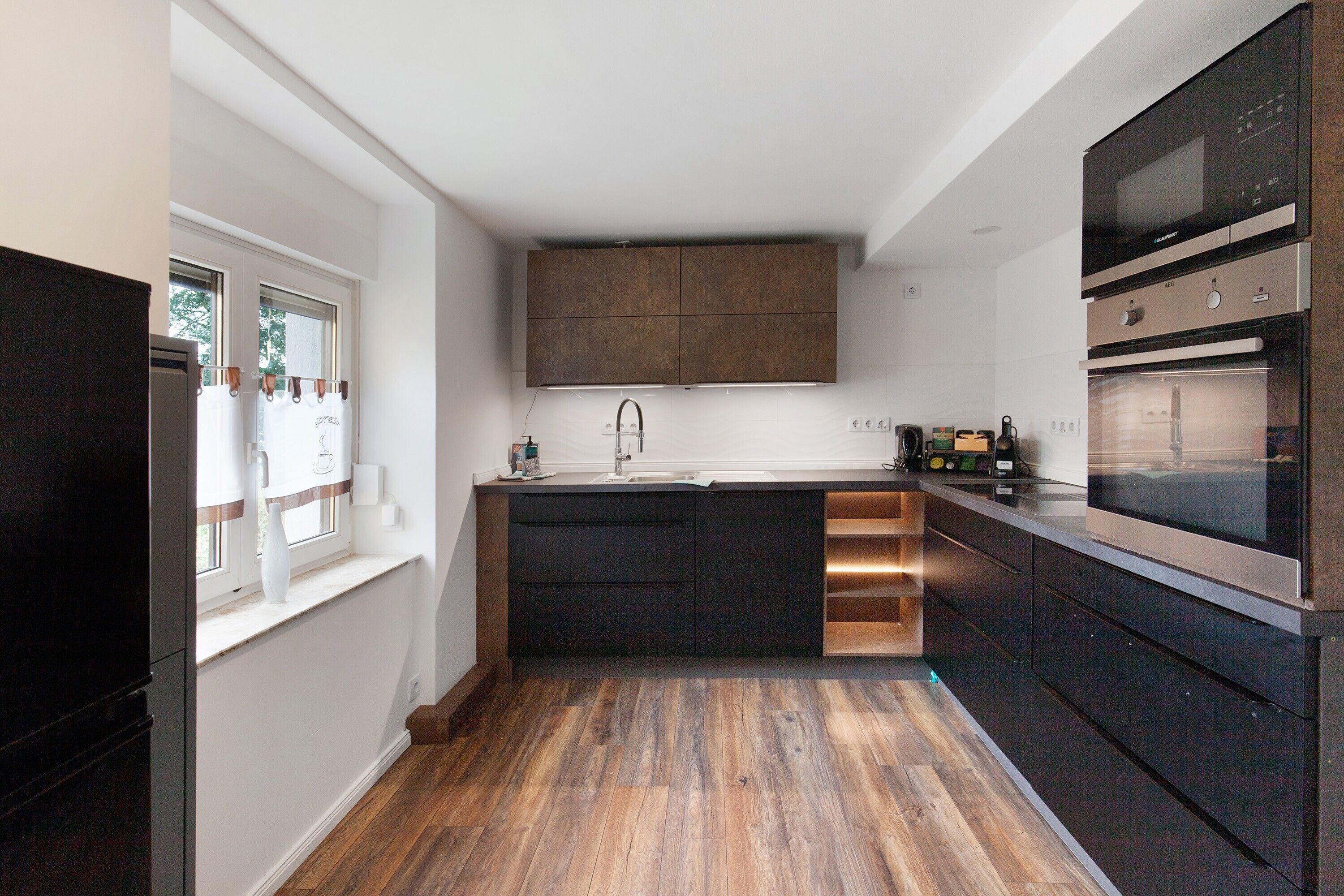 A modern kitchen with a central island, built-in appliances, and a window with curtains.