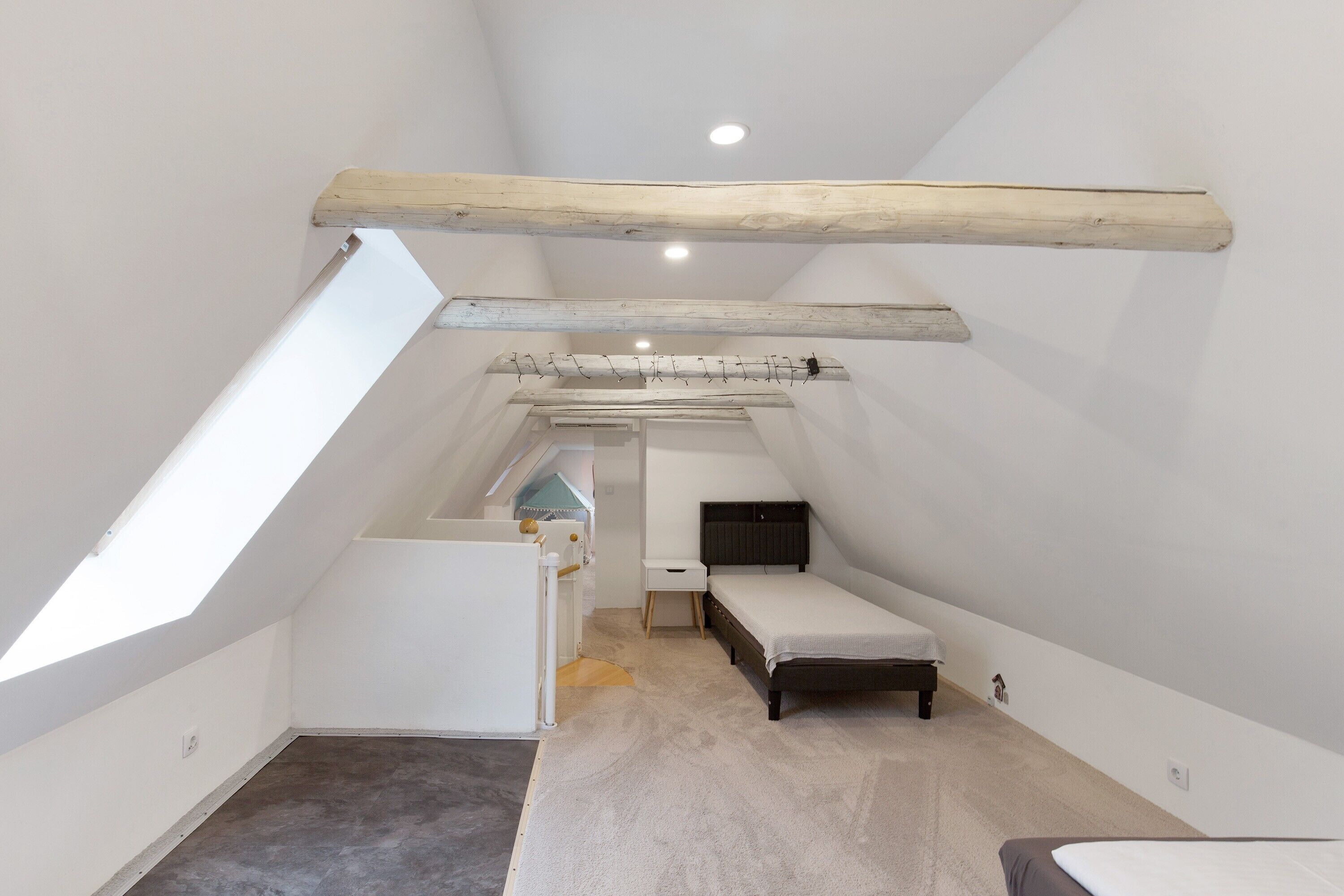 A small attic bedroom with a sloped ceiling, a single bed, a small table, and a window.