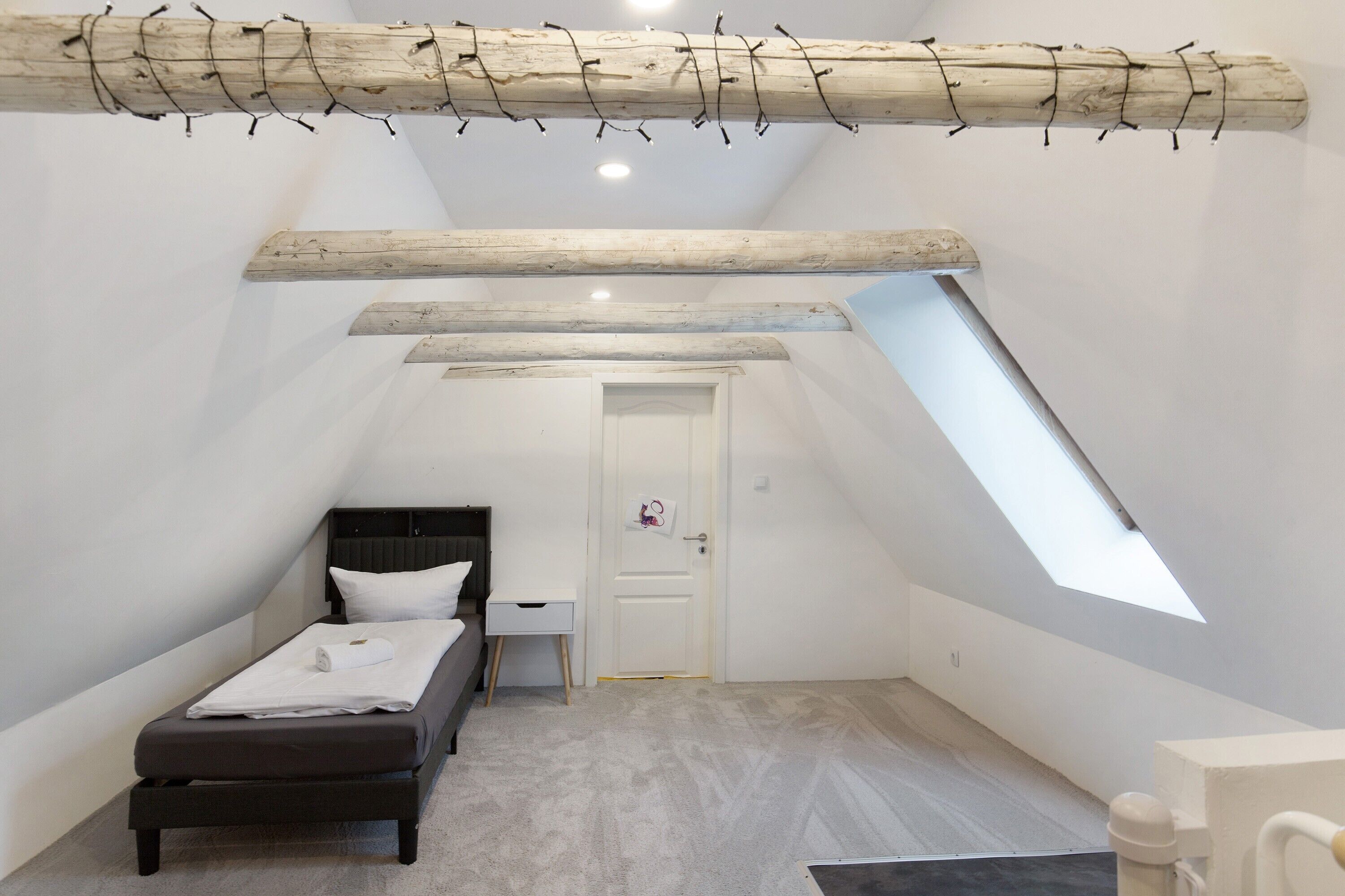 A small, modern bedroom with a sloped ceiling, a bed, a desk, and a skylight.
