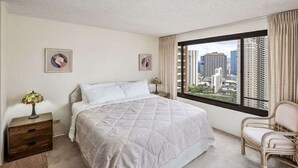 Una camera d'albergo con un letto grande, una sedia, un comodino e una finestra con vista sulla città.