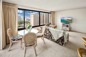 A room with a large window, a round table, wicker chairs, a sofa with a floral cover, and a television on a stand. - The Moana Horizon Suite Ala Moana 28th Floor (Honolulu)
