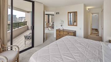 A hotel room with a bed, a chair, a dresser, and a balcony with a view of the city.