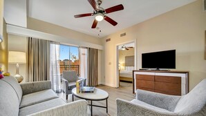 Una habitación de hotel moderna con sofá, sillón y televisor sobre un mueble de madera.