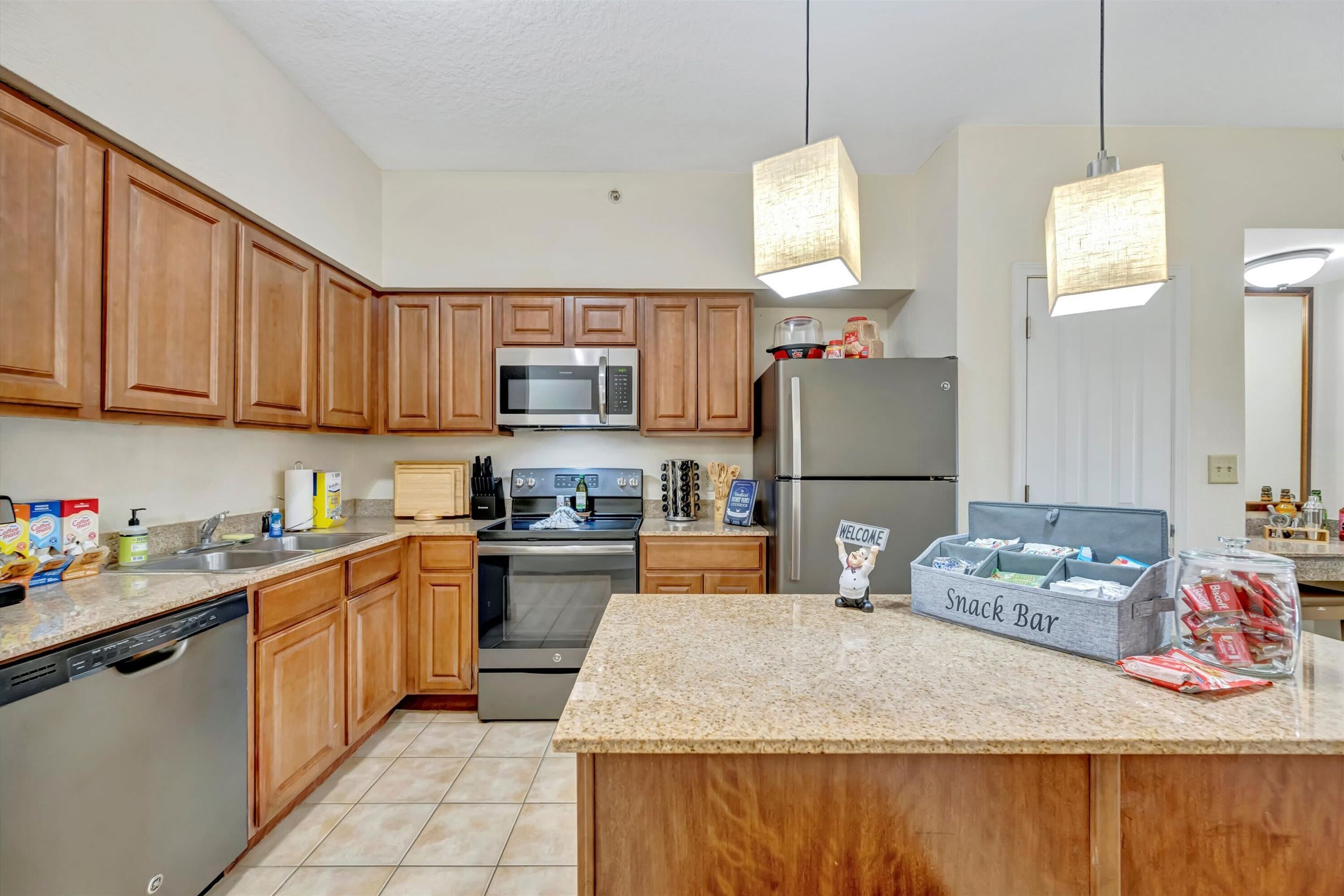 A modern kitchen with wooden cabinets, stainless steel appliances, a granite countertop, and a snack bar.