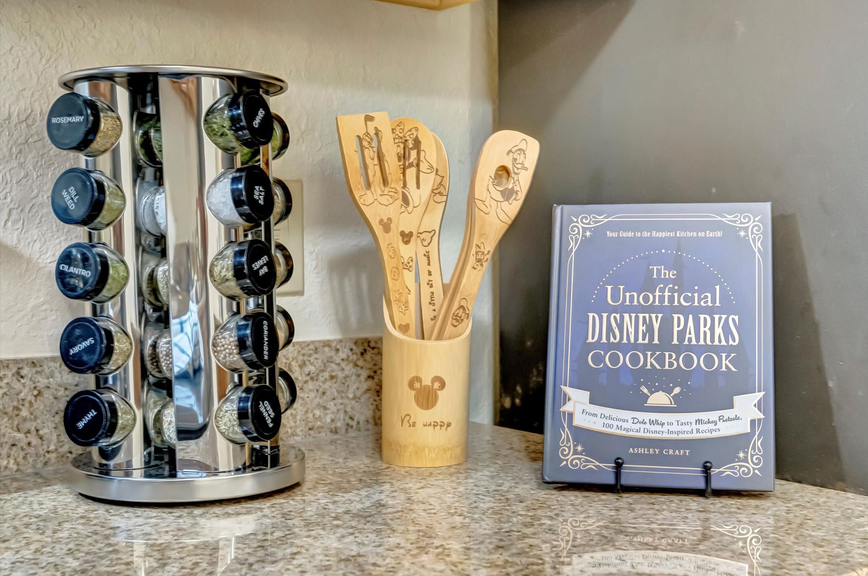 Una encimera de cocina con un especiero, utensilios de madera y un libro de recetas.