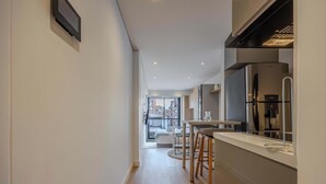 Un couloir étroit mène à un balcon d’où l’on peut admirer les bâtiments environnants. On y trouve également une petite cuisine équipée d’un réfrigérateur et un coin repas avec des tabourets.