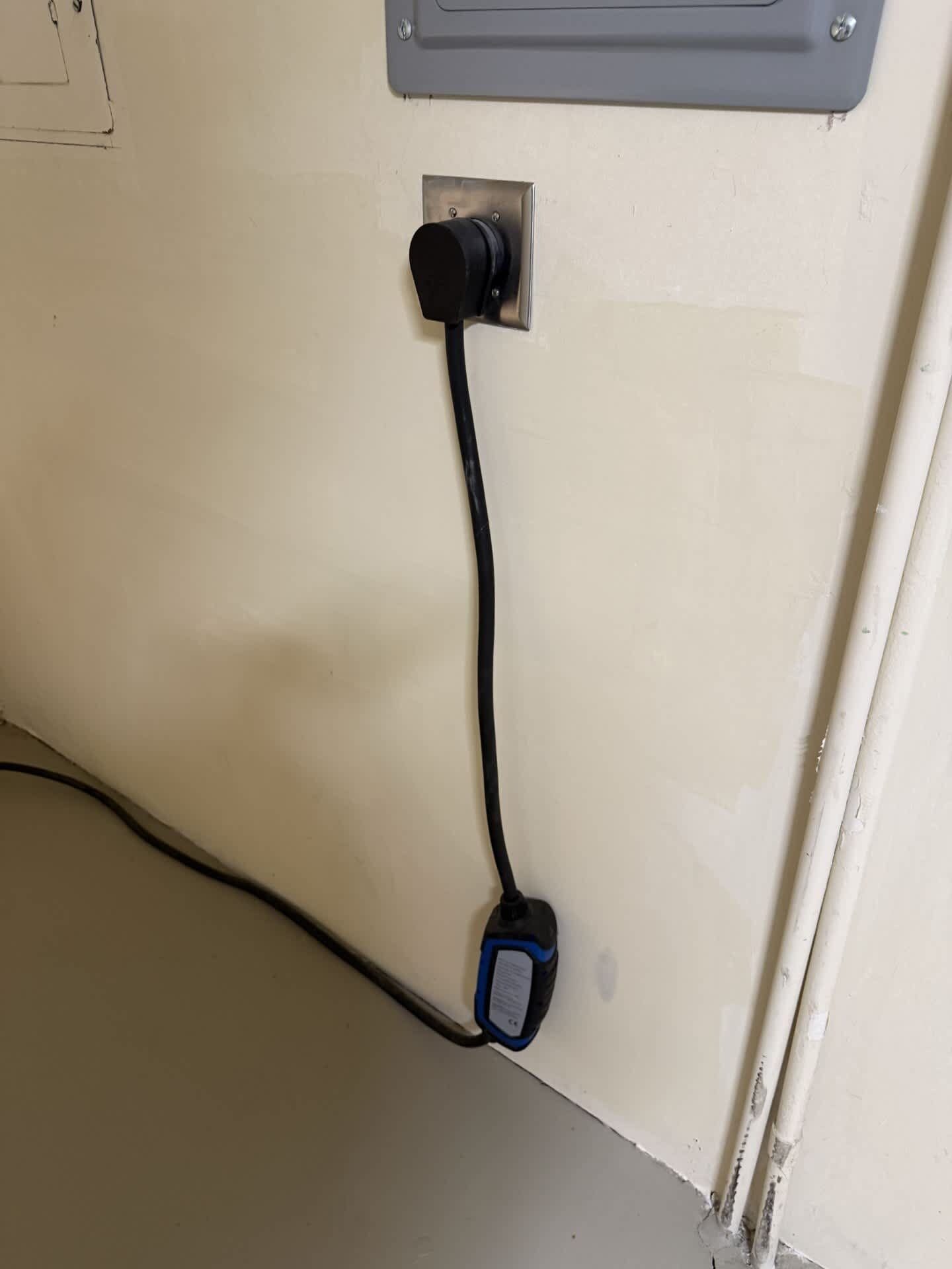 Presta d'electricitat fixada a la paret amb un cable negre connectat.