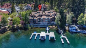 An aerial view of a modern hotel with multiple floors, a dock with boats, and a forested backdrop. - Village Lakefront Paradise (Lake Arrowhead)