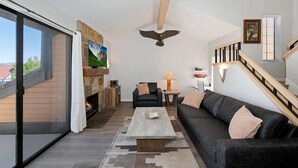 A modern living room with a fireplace, a sofa, a coffee table, and a staircase. - Village Lakefront Paradise (Lake Arrowhead)