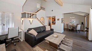 A modern living room with a staircase, a sofa, a coffee table, and a dining area. - Village Lakefront Paradise (Lake Arrowhead)