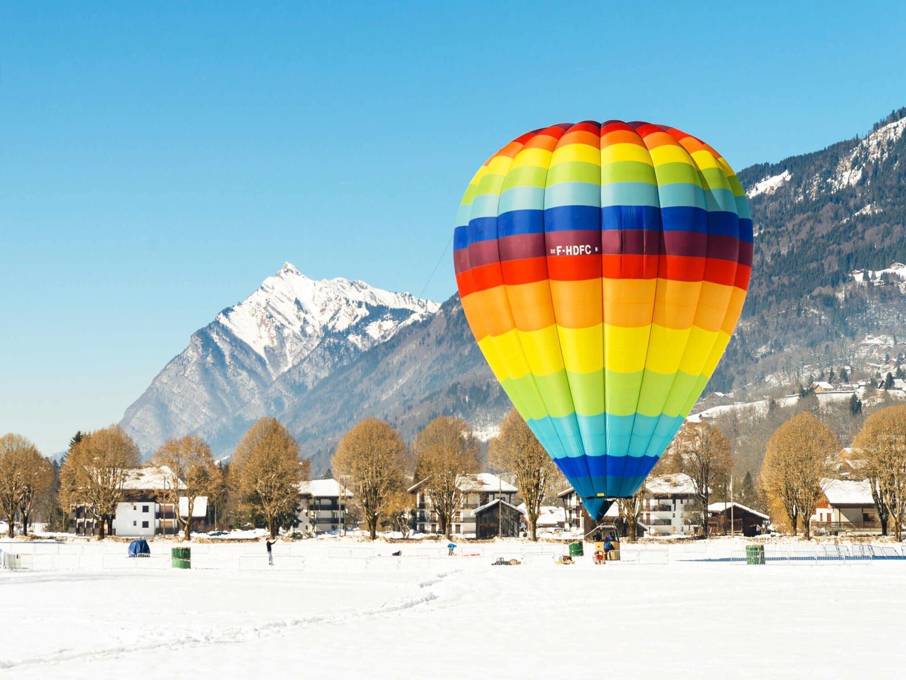 Un ballon à air chaud aux couleurs vives, évoluant dans un paysage enneigé avec des montagnes en arrière-plan.