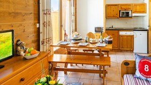 A cozy room with wooden walls, a dining table set for four, a kitchen with wooden cabinets, and a bed with a striped pillow. - Samoens Village Apartment for 4 (Samoëns)