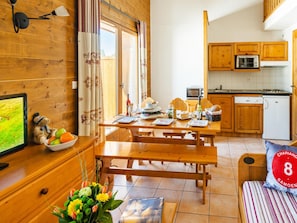 A cozy room with wooden walls, a dining table set for four, a kitchen with wooden cabinets, and a bed with a striped pillow. - Samoens Village Apartment for 4 (Samoëns)