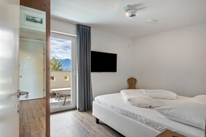 Una habitación de hotel con una cama, televisión montada en la pared y un balcón con vistas.
