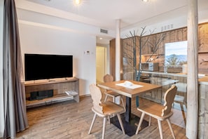 Ein modernes Wohnzimmer mit Flachbildfernseher, Holzmöbeln und Blick durch eine Glaswand.