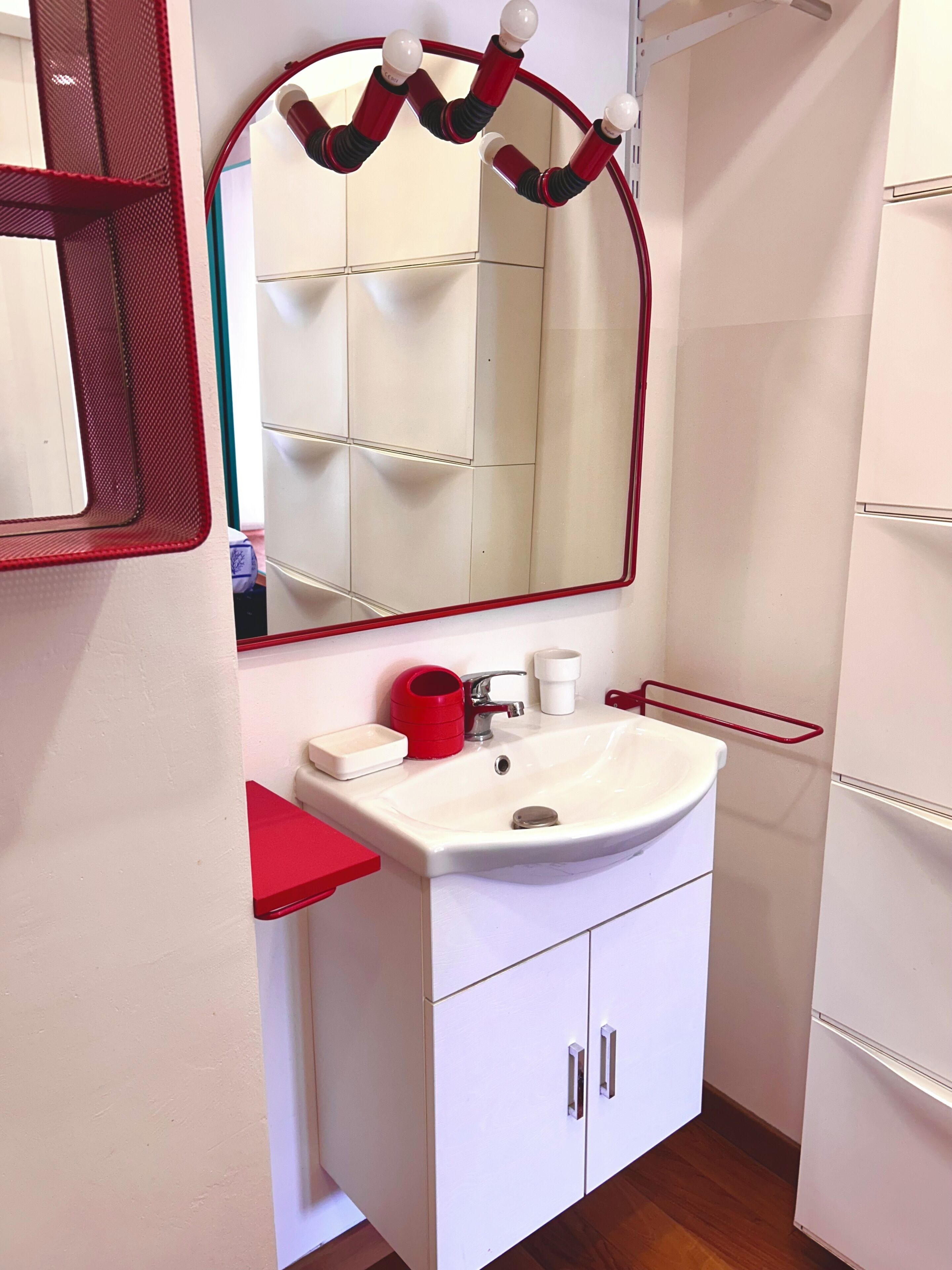 A bathroom with a white sink, red towel holder, and a mirror with lights.
