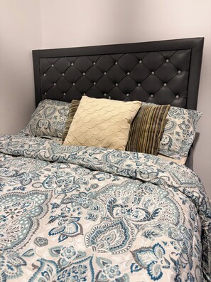 Ein Bett mit einem gemusterten Duvet, einem gesteppten Kopfteil und mehreren Kissen.