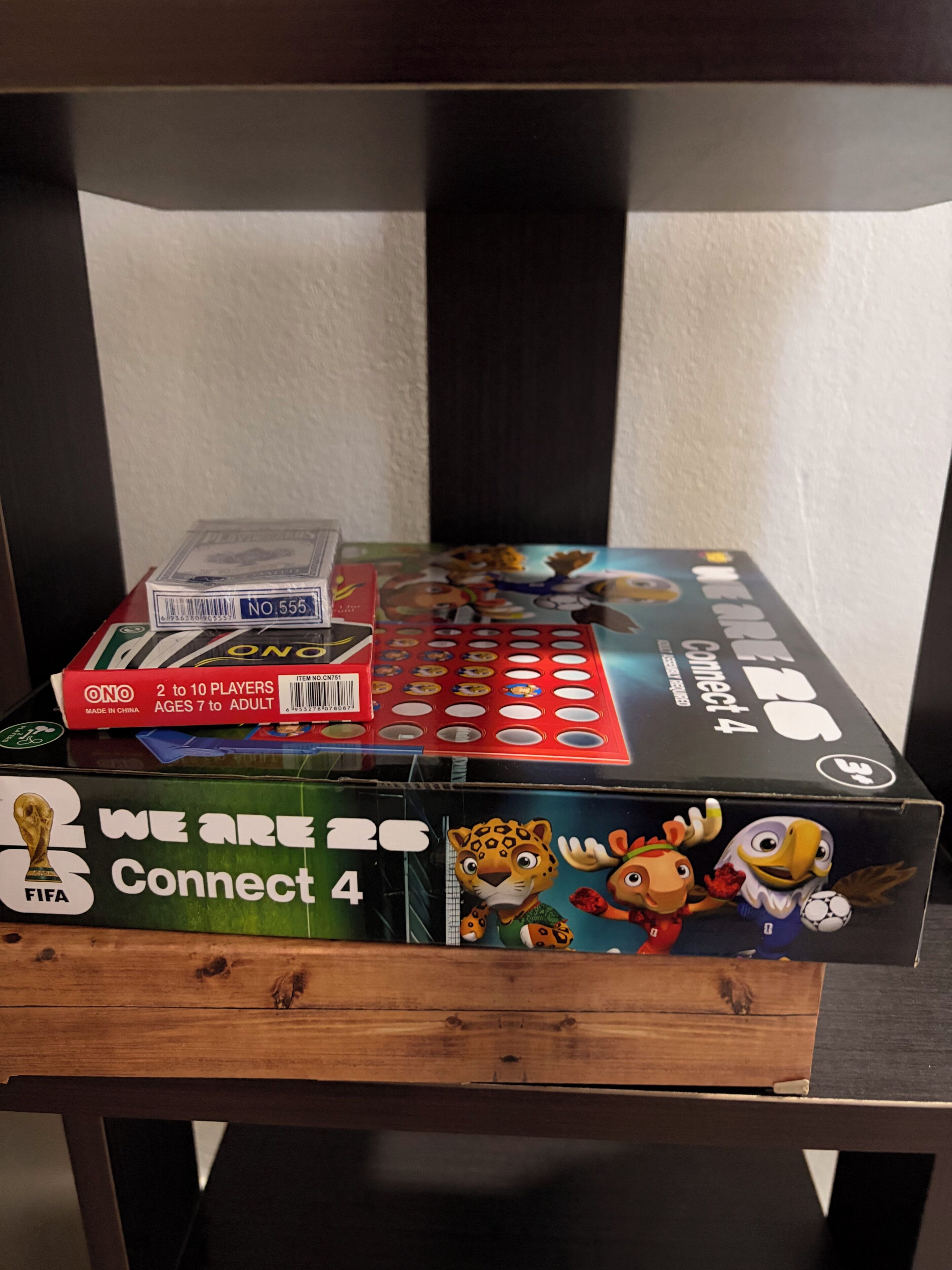 Une étagère en bois avec un jeu de société, une boîte étiquetée « We Are 26 Connect 4 » et une maquette du trophée de la Coupe du monde de la FIFA.