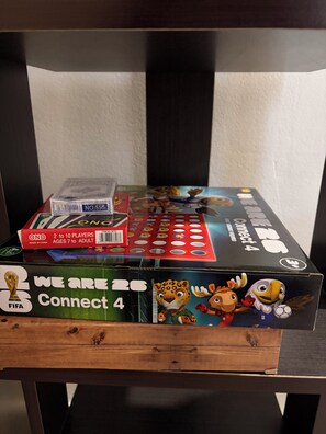 Ein Holzregal mit einem Brettspiel, einer Schachtel mit dem Aufdruck 'We Are 26 Connect 4' und einer Weltmeisterschaftstrophäe der FIFA.