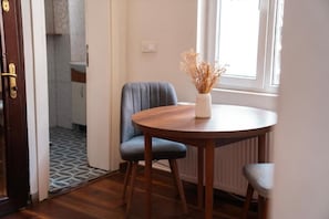 Una stanza con un tavolo rotondo in legno, due sedie, un vaso con fiori secchi, una finestra e una porta che dà su un bagno.