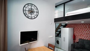 A compact living space with a wall-mounted clock, a flat-screen TV, a dining table, a sofa, and a laundry area. - Taxim no 1 Suites Istanbul (Istanbul)