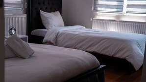 A bedroom with two beds, a nightstand with an alarm clock, and a window with blinds. - Taxim no 1 Suites Istanbul (Istanbul)