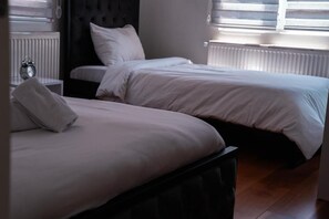 Ein Schlafzimmer mit zwei Betten, einem Nachttisch mit Wecker und einem Fenster mit Jalousien.