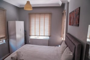 Ein Schlafzimmer mit Bett, Kleiderschrank, Heizkörper und einem Fenster mit Jalousien.