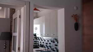 Une cuisine avec des meubles blancs, un pare-feu en carrelage et une chaise noire.