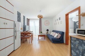 Ein modernes Wohnzimmer mit Essbereich, einem blauen Sofa, einem Holztisch und einer Küchenzeile mit einer Mikrowelle.