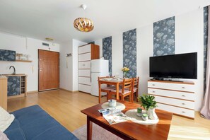 Ein modernes Wohnzimmer mit Essbereich, Fernseher und einer Küche im Hintergrund.