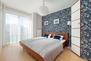 Ein Schlafzimmer mit Bett, Kleiderschrank und einem Fenster mit durchscheinenden Vorhängen.