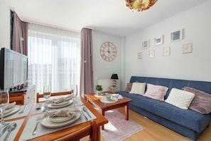 A modern living room with a dining area, a blue sofa, a clock, and framed pictures on the wall. - Cozy Apartment in the Heart of Świnoujście | Near Plac Wolności (Świnoujście)