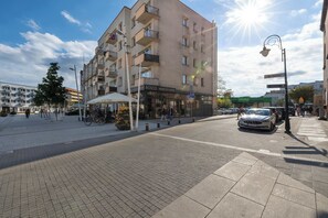 A multi-story building with balconies, a restaurant, and a street with pedestrians and vehicles. - Cozy Apartment in the Heart of Świnoujście | Near Plac Wolności (Świnoujście)
