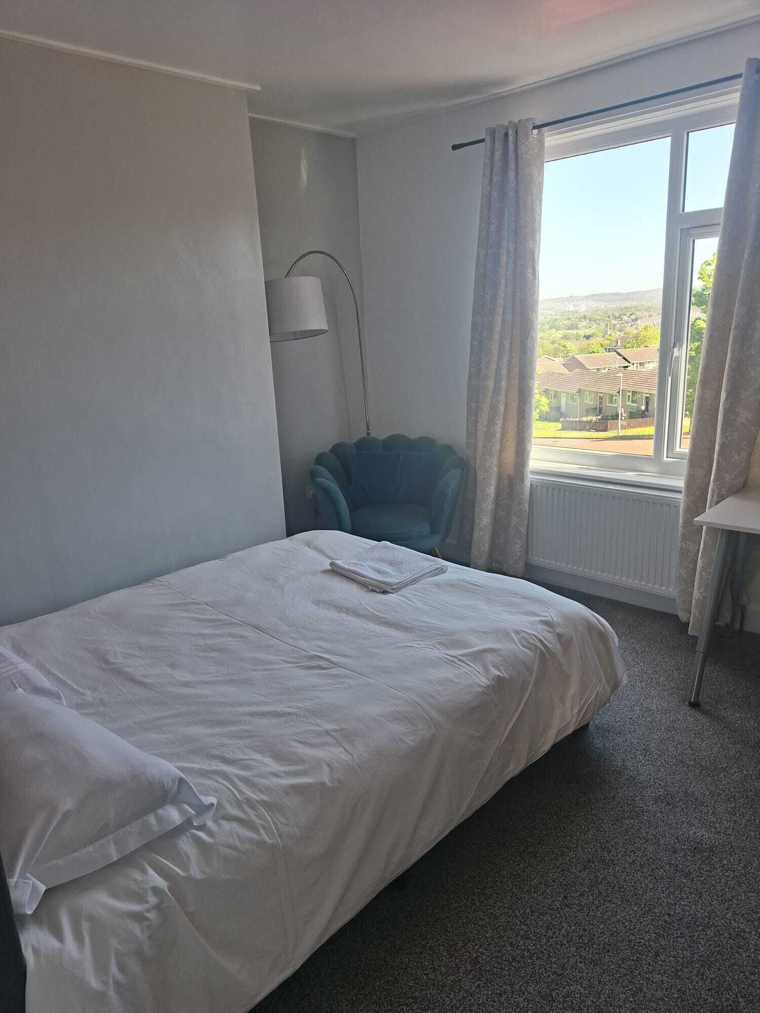 Habitació d'hotel amb un llit individual, una cadira, una làmpada i una finestra amb cortines.