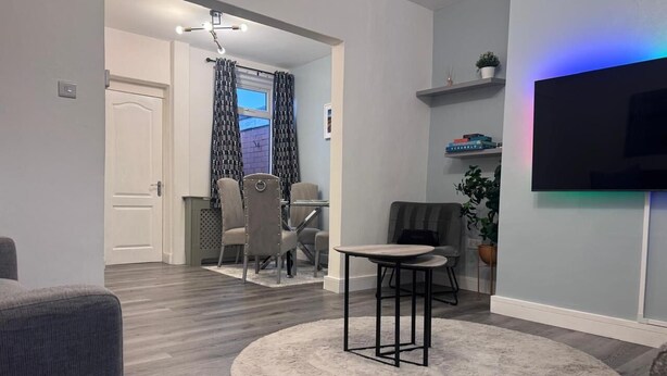 A living room with a round rug, a TV mounted on the wall, and a dining area with chairs and a table.