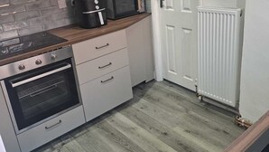 A kitchen with white cabinets, a microwave, a kettle, an oven, and a radiator.