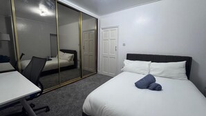 A hotel room with a bed, a desk, a chair, a wardrobe, and a door.