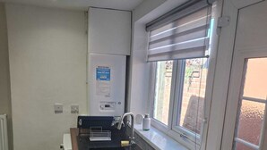 A compact kitchen with a built-in sink, a window with blinds, a refrigerator, and a wall-mounted registration sign.