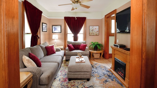 A living room with a sofa, ottoman, ceiling fan, fireplace, and a television. - Historic, dog friendly, 2-BR cottage, walking distance to downtown Baraboo (Baraboo)