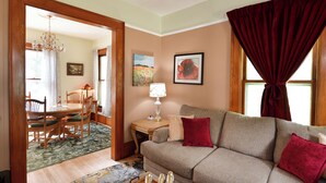 A living room with a sofa, a dining table with chairs, a chandelier, and a window with curtains. - Historic, dog friendly, 2-BR cottage, walking distance to downtown Baraboo (Baraboo)