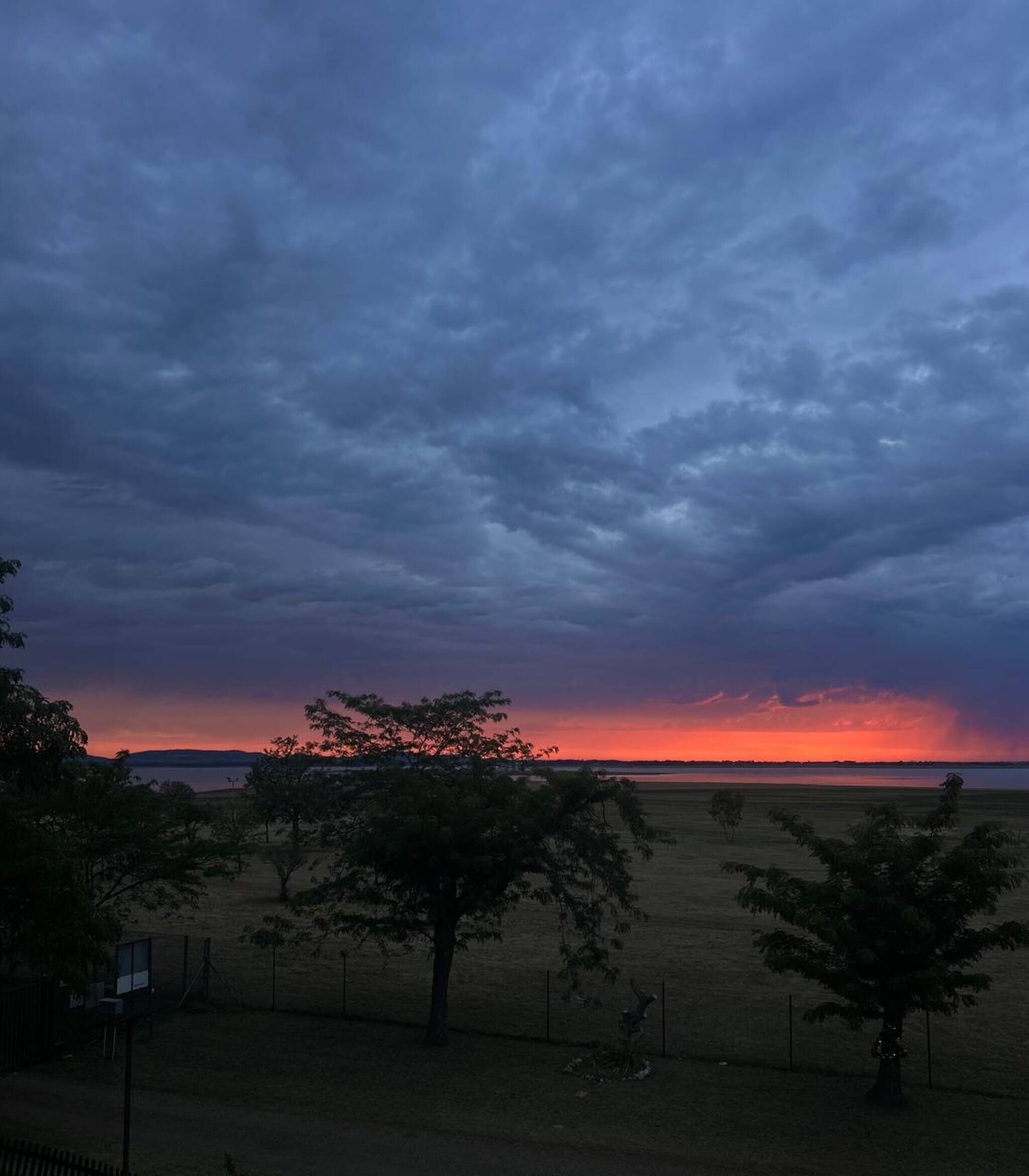 A landscape with a body of water, trees, and a fence.