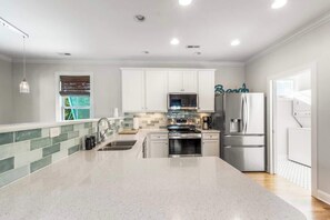 A modern kitchen with white cabinets, stainless steel appliances, and a large island. - Coastal Gem, by the beach and lake (Carolina Beach)