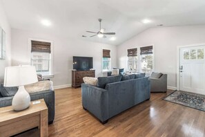 A living room with a sofa, a television, a ceiling fan, and a door. - Coastal Gem, by the beach and lake (Carolina Beach)