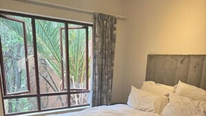Ein Schlafzimmer mit großem Fenster, einem Bett mit weißer Bettwäsche und einem flauschigen, grauen Teppich.