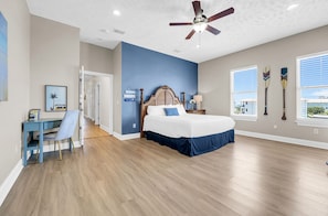 Ein Schlafzimmer mit Bett, Schreibtisch, Stuhl, Deckenventilator und Fenstern.