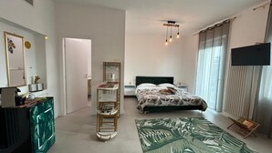 A bedroom with a bed, a TV, a shelf unit, and a window with curtains. - COMFORT ACCOMMODATION SUITE≤ CAMERE (Bergamo)