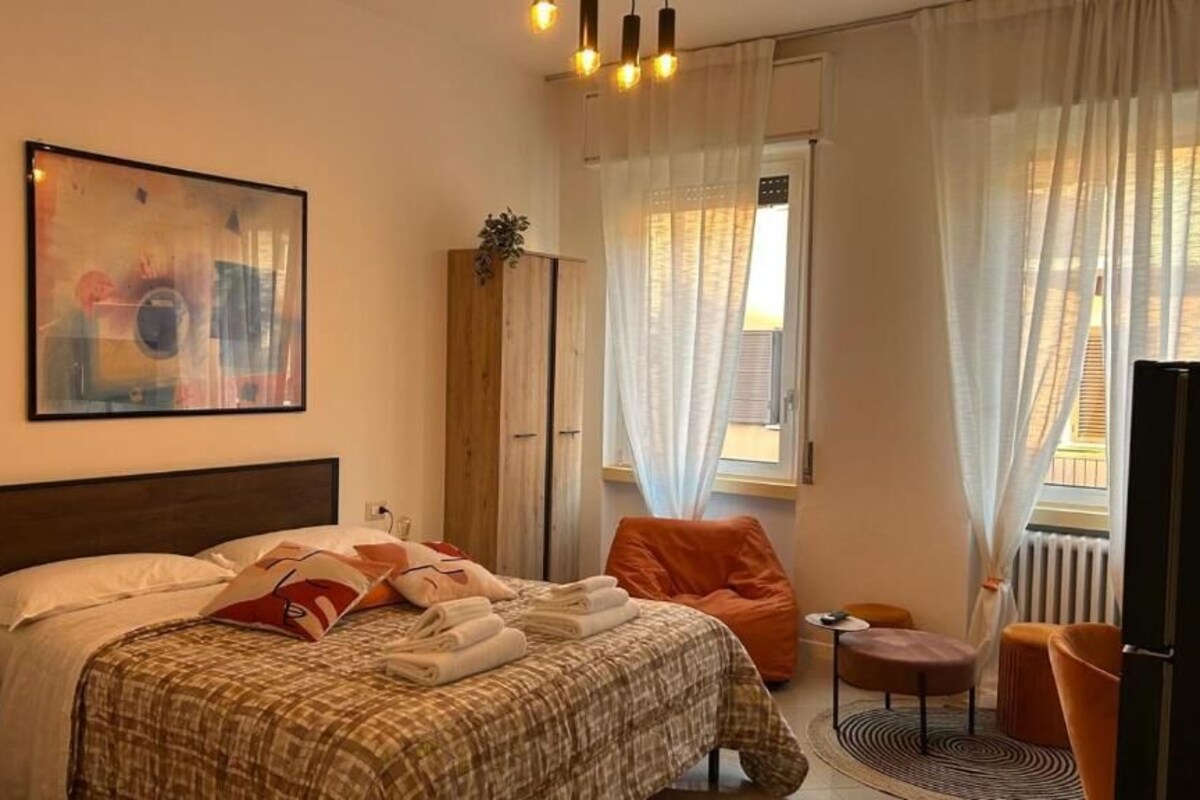 Una camera d'albergo con un letto, una sedia, un tavolino, un armadio e una finestra con tende.