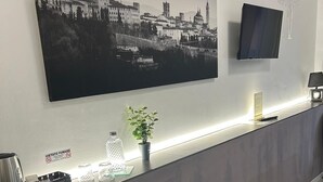 A reception desk with a cityscape painting, a TV, and a plant. - COMFORT ACCOMMODATION SUITE≤ CAMERE (Bergamo)