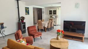 A living room with a sofa, armchair, TV, and a dining area with chairs and a table. - Gîte "la Galinette" in village center, air-conditioned with swimming pool. (Vallon-Pont-d'Arc)